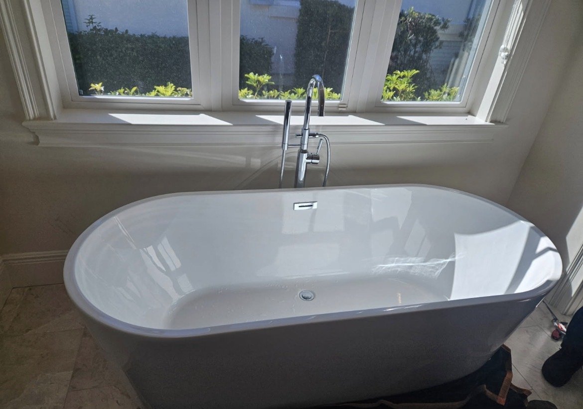Freestanding bathtub with a floor-mounted tub filler near a window